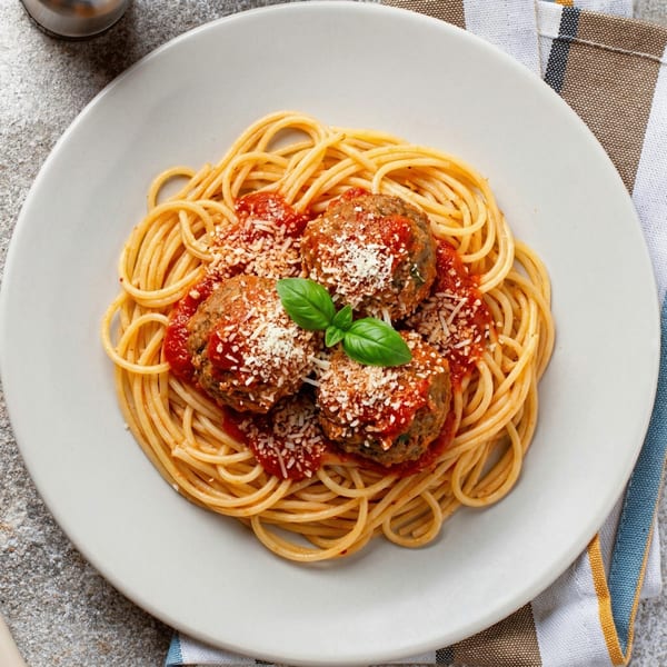 Spaghetti and meatballs with tomato sauce, grated cheese, and a basil leaf on a white plate.