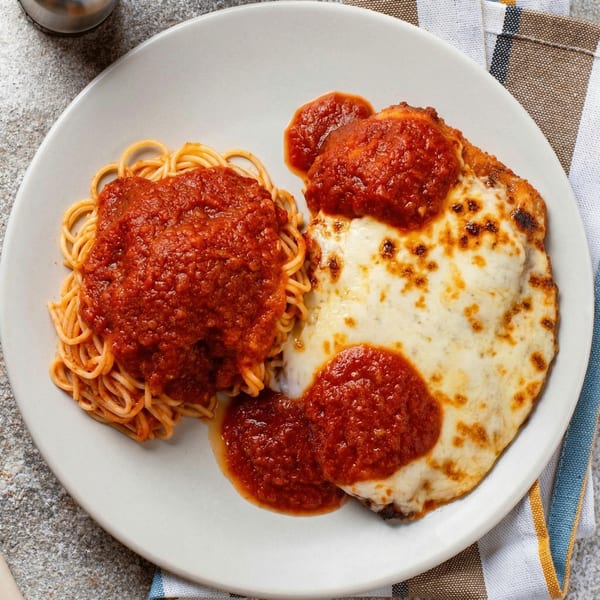 Chicken parmesan with melted mozzarella and marinara sauce, served with spaghetti on a white plate.