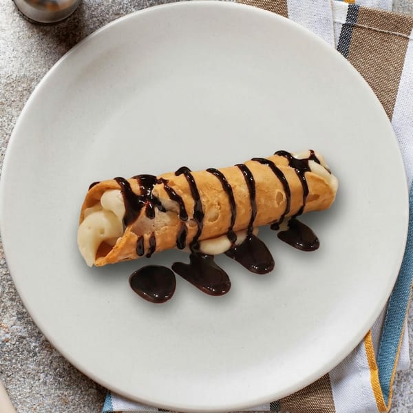 A single cannoli filled with cream and drizzled with chocolate sauce on a white plate.